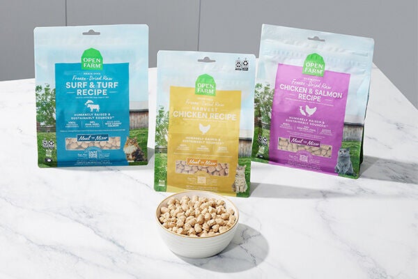 Image of three bags of freeze-dried raw cat food, one blue, one yellow, one purple on a counter with a white bowl with freeze-dried food in it.